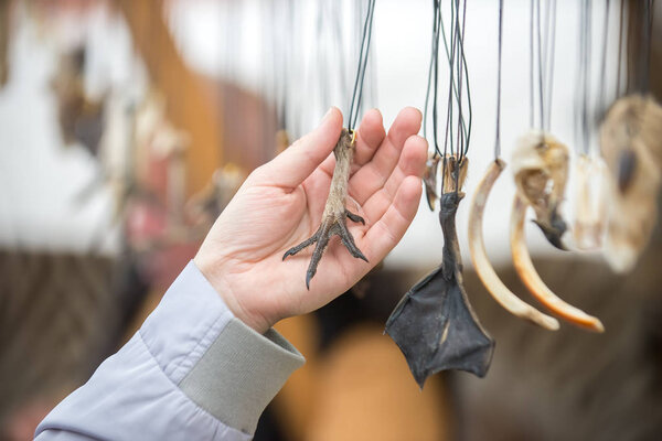 A man chooses a magic amulet from the bird's paw, different amulets hang on the laces on the stand at the fair.