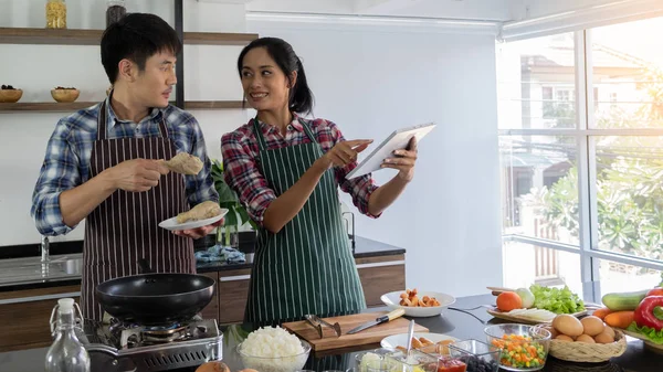 Young Asian couples are happy to cook together, two families are helping each other prepare to cook in the kitchen, Women use tablet to find recipes.