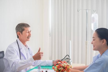 Kıdemli Asyalı doktor parmak kaldırdı ve tedavi raporu kontrol ederken gülümseme ile kadın hasta bakmak, doktor ofisinde