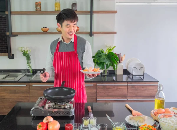 Asian young man in Red apron, happiness with Smiling. Holding fried sausage on dishes for  food in the kitchen. and people concept, copy space.