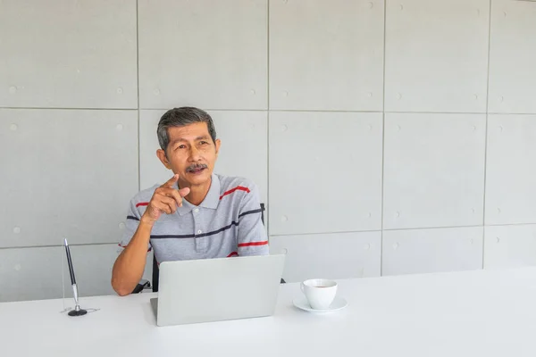 亚洲资深商人 想点什么 前面在桌子上 有白色的咖啡杯和笔记本电脑 在办公室 — 图库照片