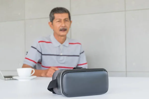 Focus of VR glasses with Asian senior man for modern technology. front on the desk there are VR glasses, in the office room