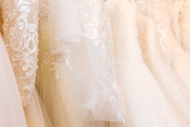 Arka planda güzel, beyaz gelinlik dokusu. Düğün elbiseleri, gelinlik salonunun iç tarafındaki askıda asılı. Tasarım, moda modern lüks detaylarıyla.