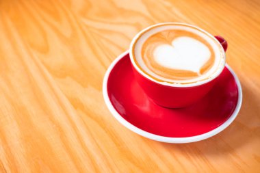 Latte sanatının ya da kapuçino kahve fincanının yakın çekimi. Tabağı ahşap masa üzerinde fotokopi alanı olan kırmızı kahve bardağı..