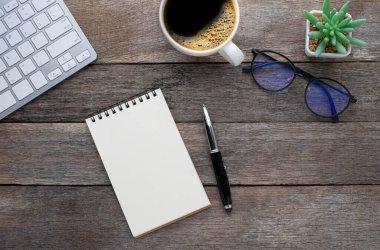 Yukarıdan bakıldığında boş bir defter, arka planda bardaklar ve kahve fincanı olan bir klavye. Evde işyeri yaratıcılığı. Fotokopi alanı olan düz alan, işletme finansmanı veya eğitim kavramı.