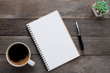 Yukarıdan bakıldığında boş bir defter ve ahşap masa arkasında kahve görünüyor. Tasarımcının evde yaratıcı çalışması için bir iş yeri. Fotokopi alanı olan düz alan, işletme finansmanı veya eğitim kavramı.