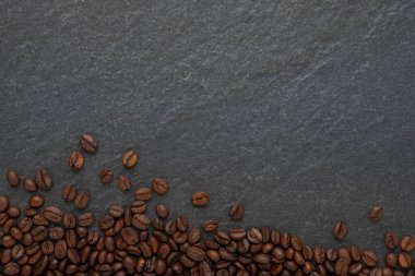 Kahverengi kahve çekirdekleri üzerinde koyu taş masa zemininde kavrulmuş. Kahvaltı menüsünün hammaddesi içkinin hoş bir aroması ve kafeinden gelen tazeliği olmasıdır. Kopyalama alanı olan düz.