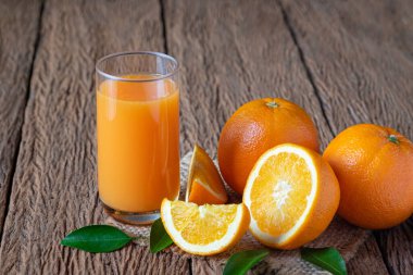 Yakın plan çekimde sıkılmış portakal suyu ve taze portakal meyveleri yarısı kesilmiş ve eski ahşap masanın üzerindeki yeşil yapraklarla dilimlenmiş. Fotokopi alanı ile organik sağlıklı konsept.