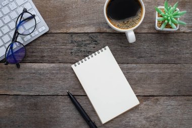 Tahta arka planda klavye, bardak ve kahve fincanı olan boş defterin üst görüntüsü. İş ve finans kavramı. Boş kopya alanı ile düz yatıyordu.