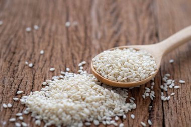 Ahşap masa arkasındaki tahta kaşıkta organik doğal beyaz susam tohumlarının yakın çekimi. Sağlıklı vejetaryen yemekleri pişirmek için organik çiğ