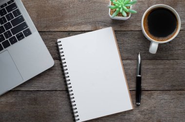 Yukarıdan bakıldığında boş bir defter, arka planda kalem ve kahve fincanı olan bir dizüstü bilgisayar. Evde işyeri yaratıcılığı. Fotokopi alanı olan düz alan, işletme finansmanı veya eğitim kavramı.