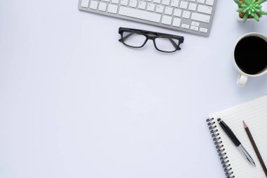 Üzerinde klavye, defter ve kahve fincanı olan beyaz ofis masasının üst görüntüsü diğer ofis malzemeleriyle dolu. İş ve finans kavramı. Boş kopya alanı ile düz yatıyordu.