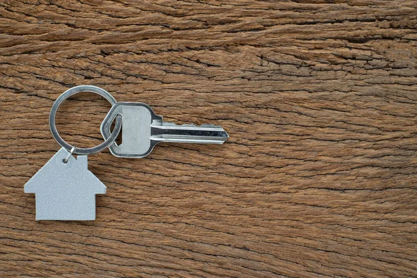 Silver key house with house shaped keychain on vintage wooden table background. Real estate concept for buying a new home with copy space.