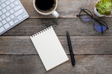 Yukarıdan bakıldığında boş bir defter, arka planda bardaklar ve kahve fincanı olan bir klavye. Evde işyeri yaratıcılığı. Fotokopi alanı olan düz alan, işletme finansmanı veya eğitim kavramı.