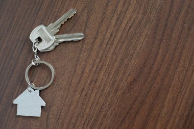 Ahşap masa arkasında ev şekilli anahtarlığı olan gümüş anahtar ev. Fotokopi alanı olan yeni bir ev almak için emlak kavramı.