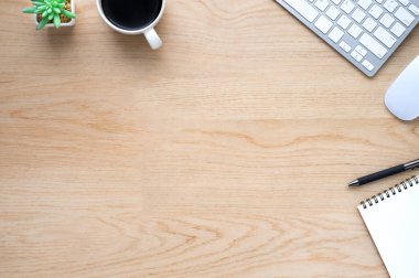 Ahşap ofis masasının üstünde klavye, defter ve kahve fincanı ve diğer ofis malzemeleri. İş ve finans kavramı. Çalışma yeri, boş kopya alanı olan düz uzanma.