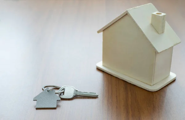 Close-up of Silver keys house with house shaped keychain and home mockup on wooden table background. Real estate concept for buying a new home with copy space.