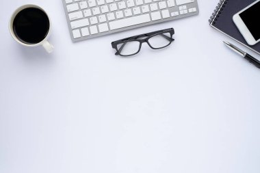 Beyaz ofis masasının üstünde klavye, defter ve kahve fincanı ve diğer ofis malzemeleri. İş ve finans kavramı. Çalışma yeri, boş kopya alanı olan düz uzanma.