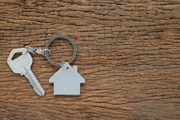 Silver key house with house shaped keychain on vintage wooden table background. Real estate concept for buying a new home with copy space.