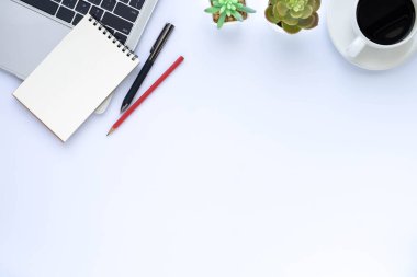 Beyaz ofis masasının üstünde dizüstü bilgisayar, defter ve kahve fincanı diğer ofis malzemeleriyle dolu. İş ve finans kavramı. Çalışma yeri, boş kopya alanı olan düz uzanma.