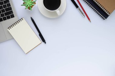 Beyaz ofis masasının üstünde dizüstü bilgisayar, defter ve kahve fincanı diğer ofis malzemeleriyle dolu. İş ve finans kavramı. Çalışma yeri, boş kopya alanı olan düz uzanma