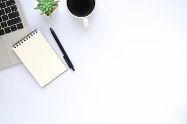 Beyaz ofis masasının üstünde dizüstü bilgisayarı, not defteri ve ekipman ofis malzemeleriyle dolu kahve fincanı var. İş ve finans kavramı. Çalışma yeri, boş kopya alanı olan düz uzanma.