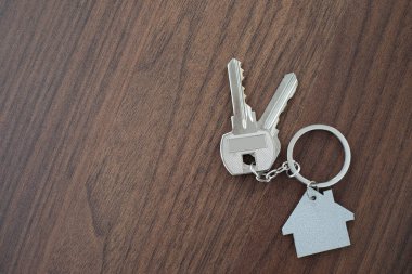 Ahşap masa arkasında ev şekilli anahtarlığı olan gümüş anahtar ev. Fotokopi alanı olan yeni bir ev almak için emlak kavramı.