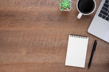 Ahşap ofis masasının üstünde dizüstü bilgisayarı, not defteri ve ekipman ofis malzemeleriyle dolu kahve fincanı var. İş ve finans kavramı. Çalışma yeri, boş kopya alanı olan düz uzanma.