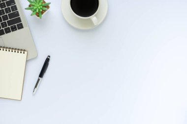 Beyaz ofis masası. Klavye bilgisayarlı çalışma alanı ve diğer ofis malzemeleriyle dolu not defteri. Kopyalama alanı olan üst görünüm, düz yatay.