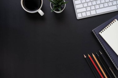 Siyah ofis masasının üstünde klavye, defter ve kahve fincanı ve diğer ofis malzemeleriyle. İş ve finans kavramı. Çalışma yeri, boş kopya alanı olan düz uzanma.