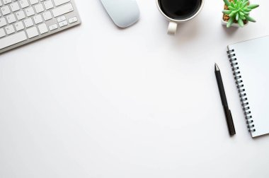 Beyaz ofis masasının üstünde klavye, defter ve kahve fincanı ve diğer ofis malzemeleri. İş ve finans kavramı. Çalışma yeri, boş kopya alanı olan düz uzanma.