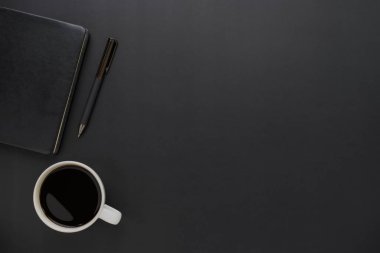 Üzerinde defter ve kalemle kahve fincanı olan koyu siyah ofis masasının üstü. İş ve finans kavramı. Çalışma yeri, boş kopya alanı olan düz uzanma.