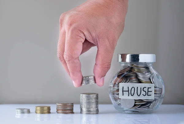 Real estate business investment and finance accounting concept. Hand putting coin into stack step up growing growth with coins in glass bottle. Saving money for buying a new house.