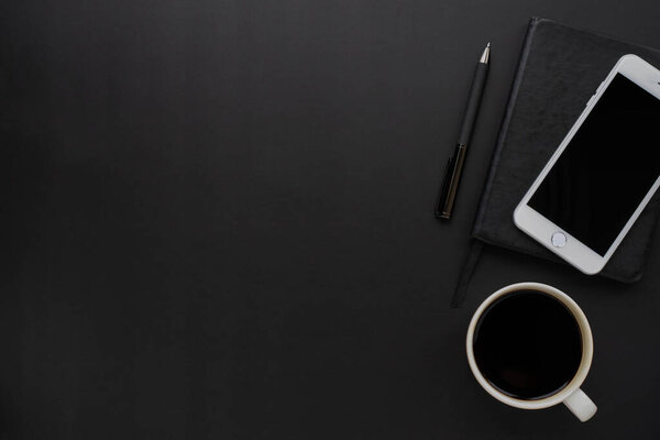 Top view above of Black office desk table with mobile phone, notebook and coffee cup with equipment other office supplies. Business and finance concept. Workplace, Flat lay with blank copy space.