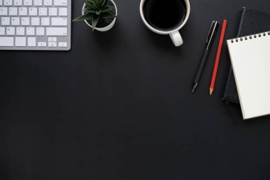 Siyah ofis masasının üstünde klavye, defter ve kahve fincanı ve diğer ofis malzemeleriyle. İş ve finans kavramı. Çalışma yeri, boş kopya alanı olan düz uzanma.