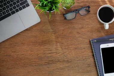 Ahşap ofis masasının üstünde dizüstü bilgisayarı ve diğer ofis malzemeleriyle dolu bir defter var. İş ve finans kavramı. Çalışma yeri, boş kopya alanı olan düz uzanma.