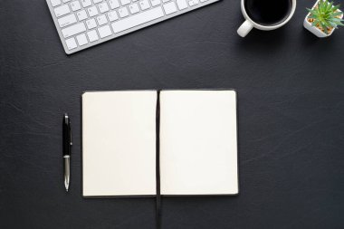 Siyah ofis masasının üstünde klavyeli, boş defterli, kahve ve diğer ofis malzemeleri. İş ve finans kavramı. Çalışma yeri, boş kopya alanı olan düz uzanma.