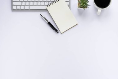 Klavyeli beyaz ofis masası, defter ve kahve fincanı diğer ofis malzemeleriyle dolu. İş ve finans kavramı. İşyeri, boş fotokopi alanı olan düz bir yer. Üst görünüm