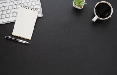 Klavyeli siyah deri ofis masası, defter ve diğer ofis malzemeleriyle dolu kahve fincanı. İş ve finans kavramı. İşyeri, boş fotokopi alanı olan düz bir yer. Üst görünüm