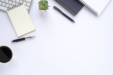 Beyaz ofis masasının üstünde klavye, not defteri ve ekipman ofis malzemeleriyle dolu kahve fincanı. İş ve finans kavramı. Çalışma yeri, boş kopya alanı olan düz uzanma.