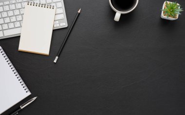 Siyah deri ofis masasının üstünde klavye, not defteri ve ekipman ofis malzemeleriyle dolu kahve fincanı. İş ve finans kavramı. Çalışma yeri, boş kopya alanı olan düz uzanma.