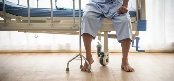 Больной или пожилой старик-азиат не мог ходить, сидя один на кровати пациента с тростью в ожидании врача и медсестры для лечения или лечения в больнице или здравоохранении. — стоковое фото