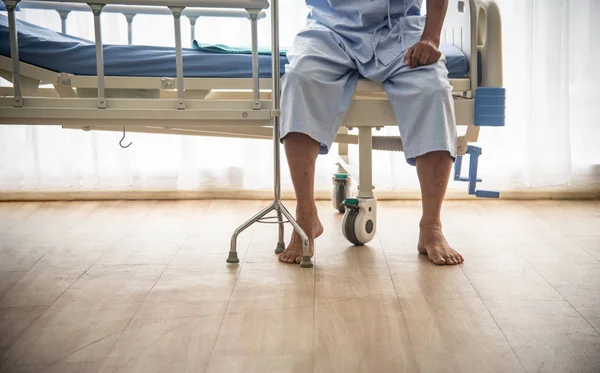 Больной или пожилой старик-азиат не мог ходить, сидя один на кровати пациента с тростью в ожидании врача и медсестры для лечения или лечения в больнице или здравоохранении. — стоковое фото
