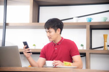 Cep telefonu rahat kırmızı t-shirt mesajlaşma ile iş adamı, kahve içme ve sandviç yeme, Genç adam mutfak odasında labtop veya bilgisayar üzerinde çalışan, çatı tarzı