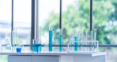 Cam eşyalar, beyaz masada mavi sıvı içeren tüp gibi laboratuvar ekipmanlarının hazırlanması. Bilimsel araştırmalarda kimya deneyi