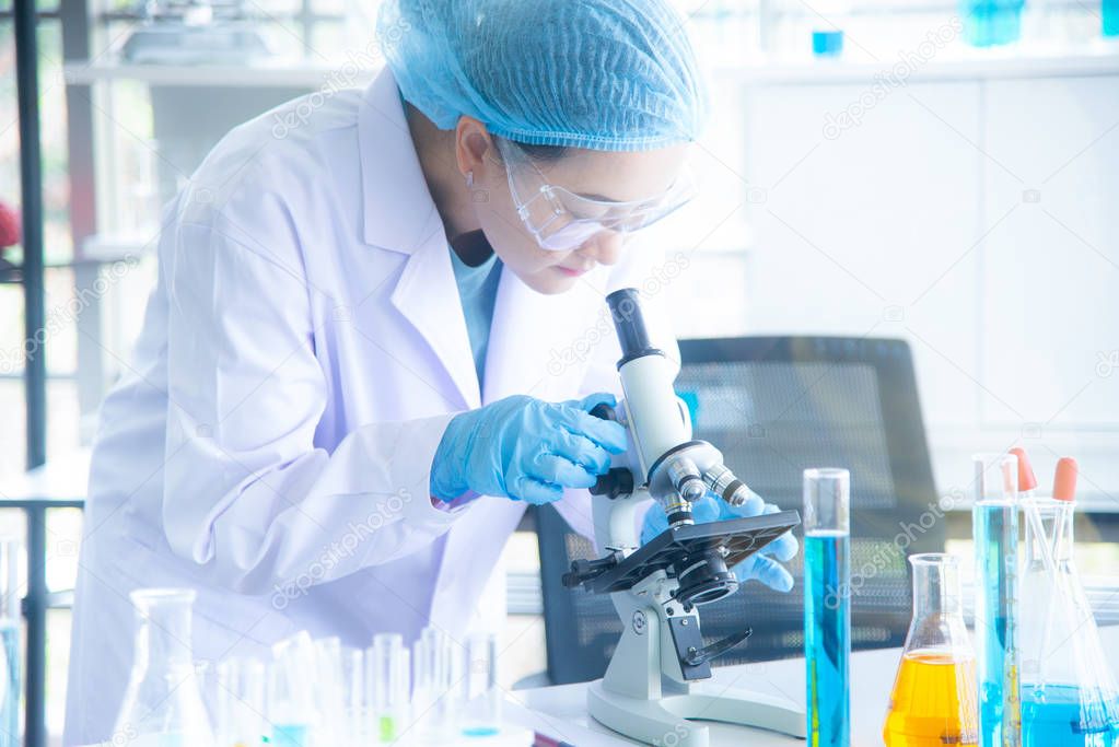 Asian woman scientist, researcher, technician, or student conducted research or experiment by using microscope which is scientific equipment in medical, chemistry or  biology laboratory