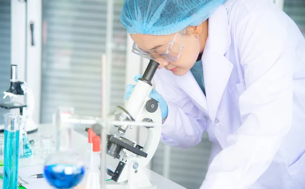 Asian woman scientist, researcher, technician, or student conducted research or experiment by using microscope which is scientific equipment in medical, chemistry or  biology laboratory