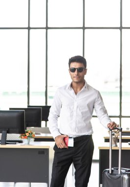 Güneş gözlüklü, valizli ve seyahat belgeli genç ve zeki işadamı uçak bileti, otel rezervasyon belgesi ve seyahat konseptli pasaport, yaz tatili konsepti, yaz tatili konsepti