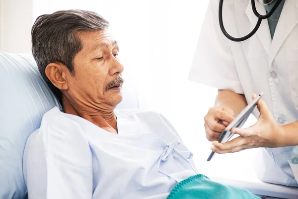Азиатская женщина профессиональный врач с планшетом посещения и диагностики старика пациента, лежащего в постели в больничном отделении. Врач имеет рутинную работу, чтобы проверить и консультировать пациента — стоковое фото