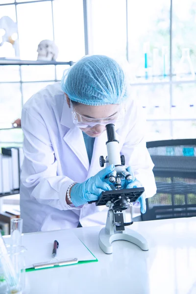 Asiatisk kvinna forskare, forskare, tekniker eller student forskat eller experimentera med Mikroskop som är vetenskaplig utrustning i medicinsk, kemi eller biologi laboratorium — Stockfoto